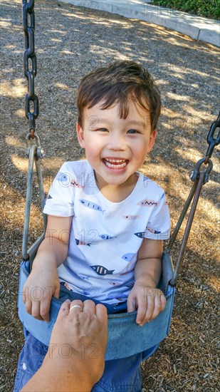 Adorable chinese and caucasian young boy having fun in the swing