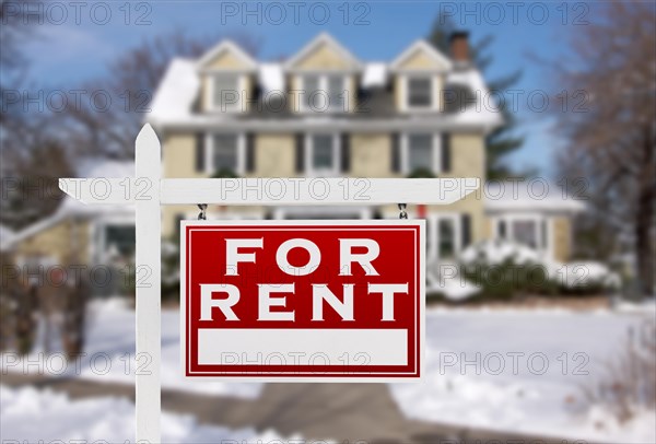 Red for rent real estate sign in front of snow covered house