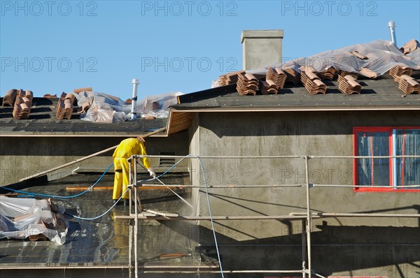 Construction worker pressure washes fresh applied surface of new home exterior