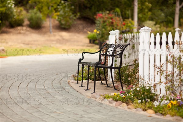 Iron park bench near a white picket fence in a rural setting