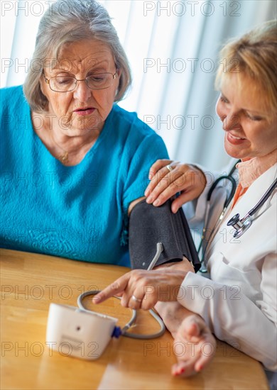 Senior adult woman learning from female doctor to use blood pressure machine