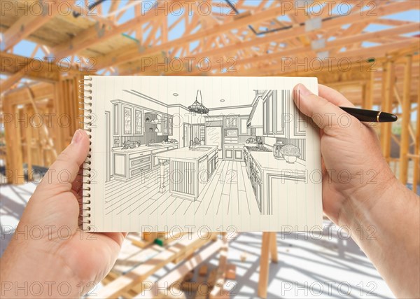 Male hands holding pen and pad of paper with custom kitchen illustration inside construction framing