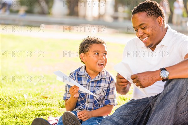 Happy african american father and mixed-race son playing with paper airplanes in the park