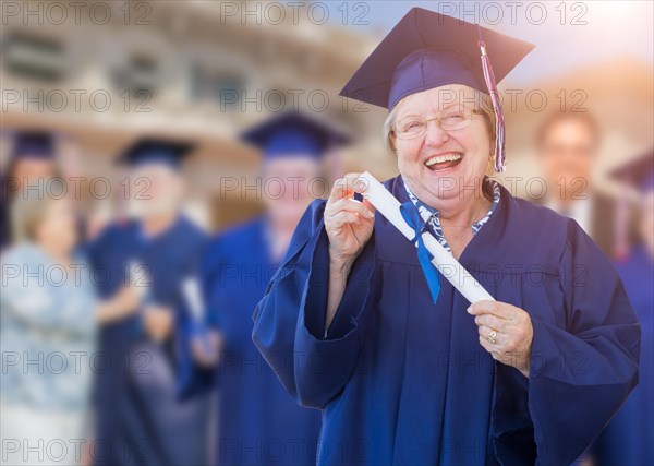 Happy senior woman in hat and gown at outdoor graduation ceremony