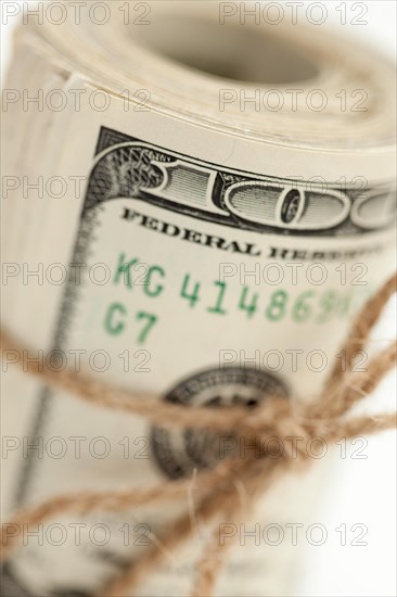 Roll of one hundred dollar bills tied in burlap string on white