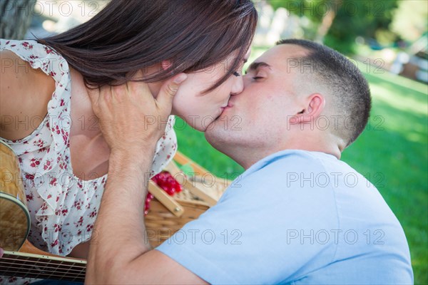 Young adult couple with guitar kissing in the park