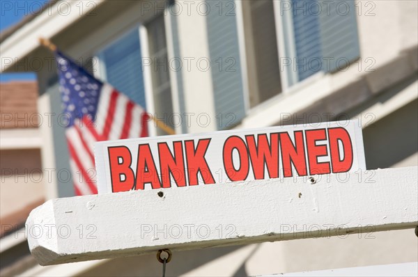 Bank owned real estate sign and house with american flag in the background