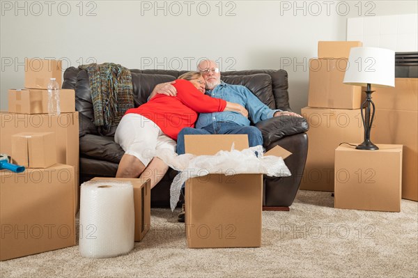 Affectionate tired senior adult couple resting on couch surrounded by moving boxes