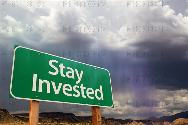 Stay invested green road sign over dramatic clouds and sky