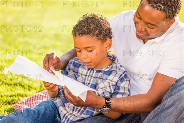 Happy african american father and mixed-race son playing with paper airplanes in the park