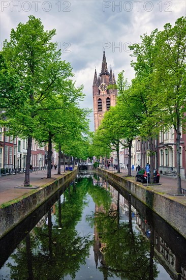 Delft canal with old houses bicycles and cars parked along and Oude Kerk Old church tower