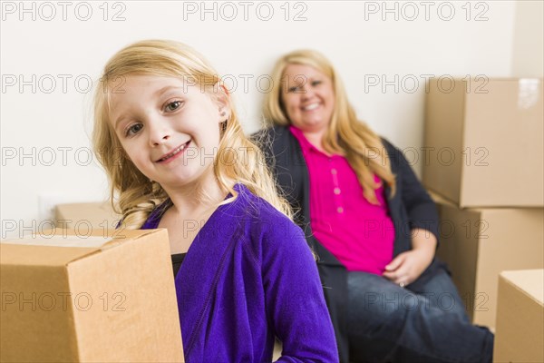 Happy young mother and daughter in empty room with moving boxes