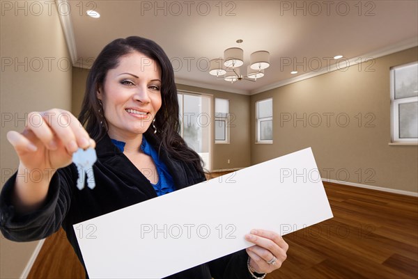 Hispanic woman with house keys and blank sign in empty room of house