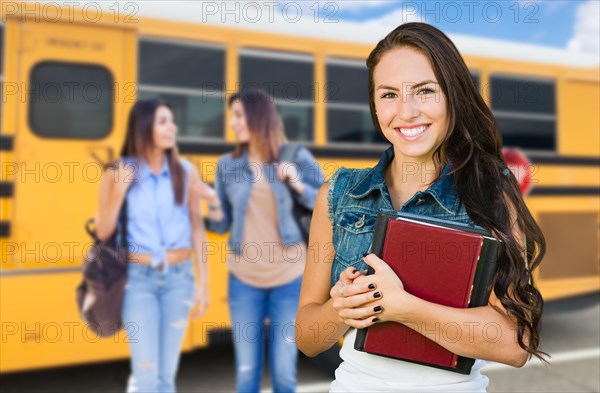 Young female student with books near school bus