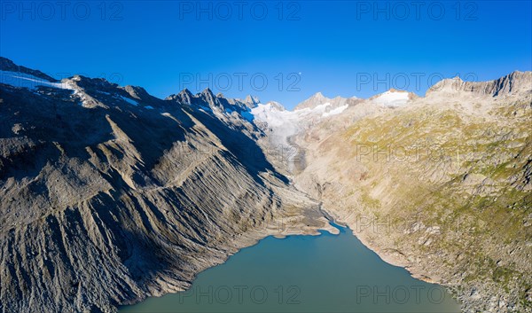 Aerial view over Lake Oberaar with the Oberaar glacier and the moon above the Bernese Alps