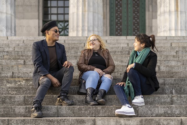 Multi ethnic group of friends sitting on some stairs having a good time chatting and laughing