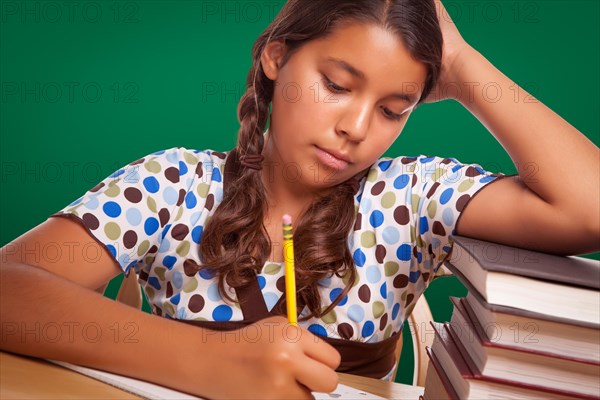 Hispanic girl student with pencil and books studying with chalk board behind
