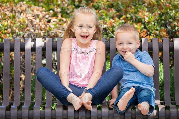 Young sister and brother having fun on the bench at the park
