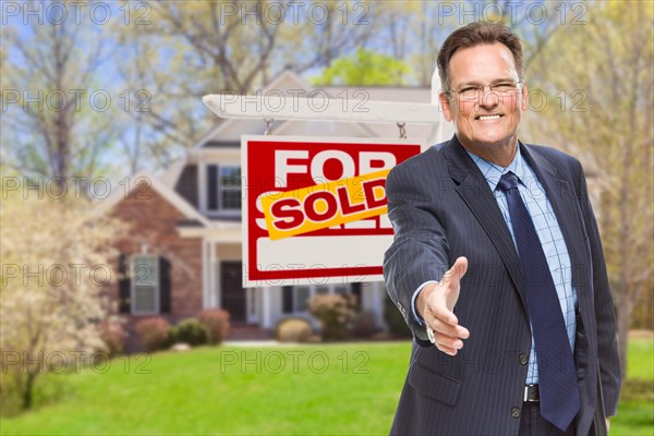 Smiling male agent reaching for a hand shake in front of beautiful house and sold real estate sign