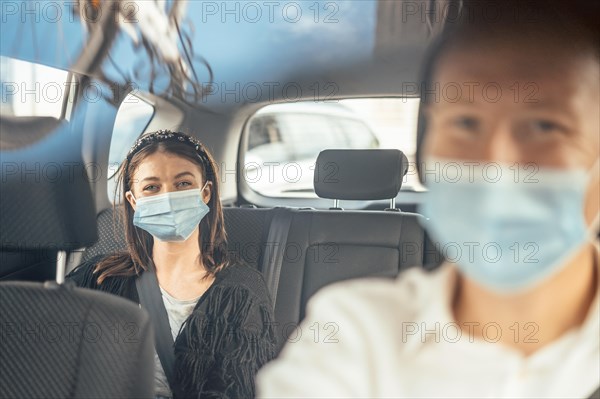 A woman wearing a protective mask sitting on the back seat of a taxi car