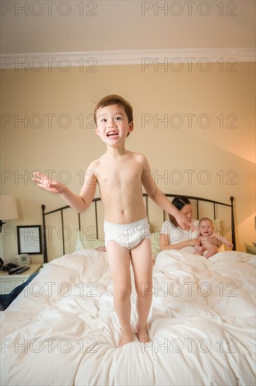 Young mixed-race chinese and caucasian boy jumping in bed with his family