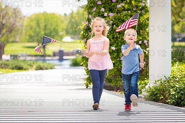 Young sister and brother waving american flags at the park