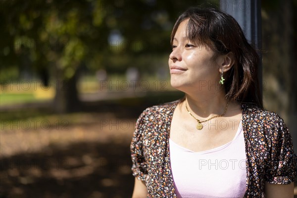 Portrait of a young Latin woman in a park leaning on a lamppost