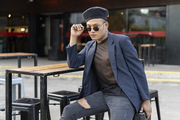 Latin gay male with makeup wearing fashion hat posing in the street