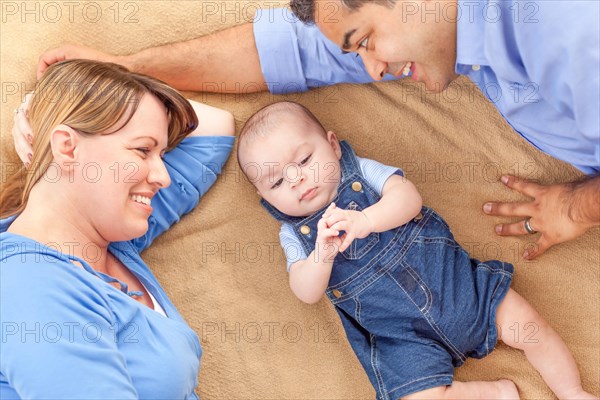 Young mixed-race couple laying with their infant on A blanket