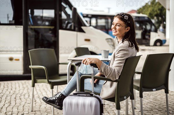 A young traveler with the luggage and protective mask sitting in the cafe and waiting for her bus to come