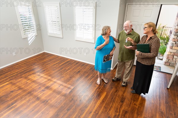 Female real estate agent handing new house keys to senior adult couple in new home