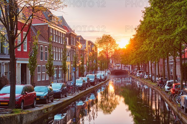 Delt canal with old houses and cars parked along on sunset. Delft