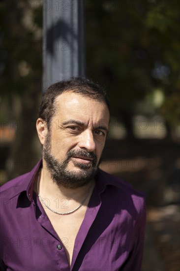 Portrait of a mature bearded man leaning on a lamp post looking at the camera