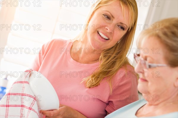 Senior adult woman and young daughter talking at sink in kitchen