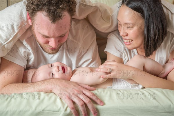 mixed-race chinese and caucasian baby boy laying in bed with his father and mother