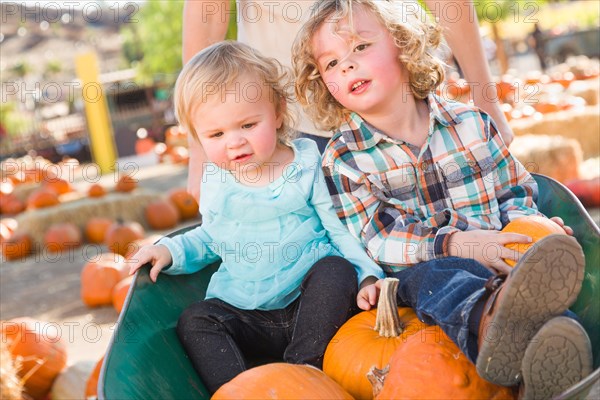 Sweet little boy plays with his baby sister in a rustic ranch setting at the pumpkin patch