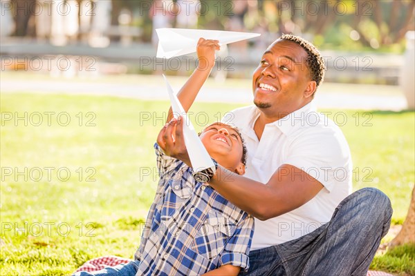 Happy african american father and mixed-race son playing with paper airplanes in the park