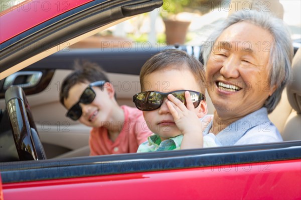 Chinese granfather and mixed-race children playing in parked car