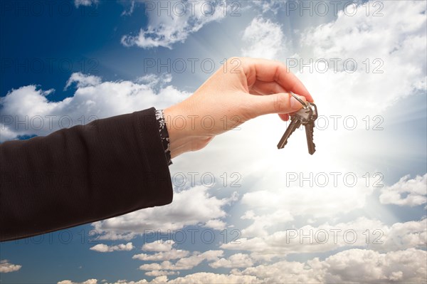 Female holding out pair of keys over dramatic clouds and sky with sun rays