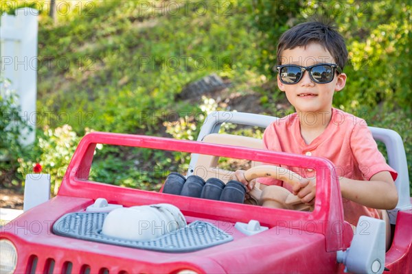 Young mixed-race chinese and caucasian boy wearing sunglasses playing in toy car