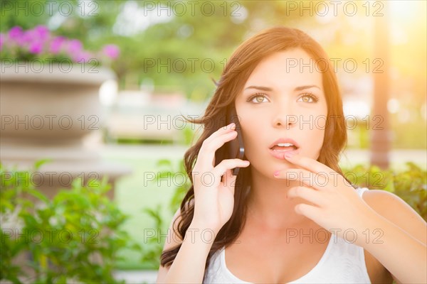 Shocked young adult female talking on cell phone outdoors on bench