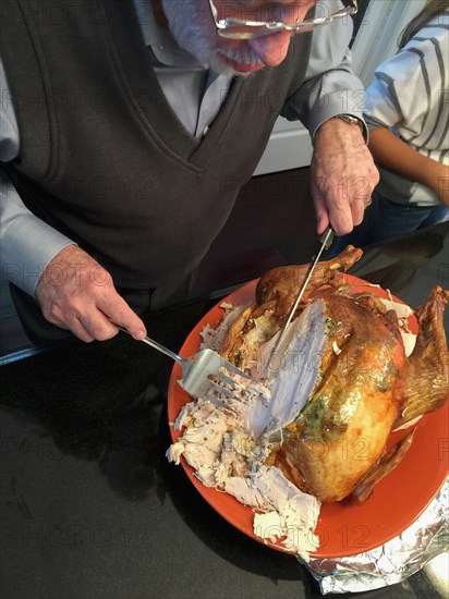 Senior adult man cutting the delicious holiday Turkey in the kitchen