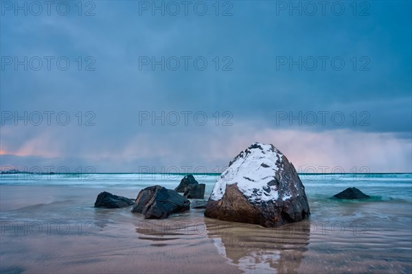 Rocks covered with snow on Norwegian sea beach in fjord in stormy weather with clouds