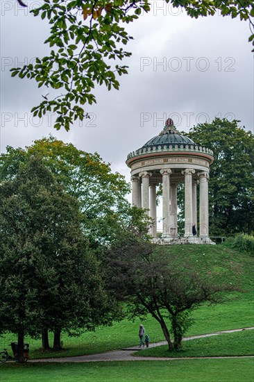 Man and child walking in the English Garden of Munich in front of the Monopteros