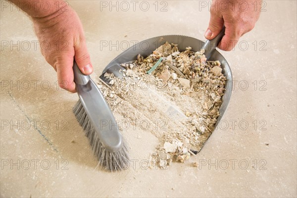 Worker picking up pile of debris on cement with brush and dust pan