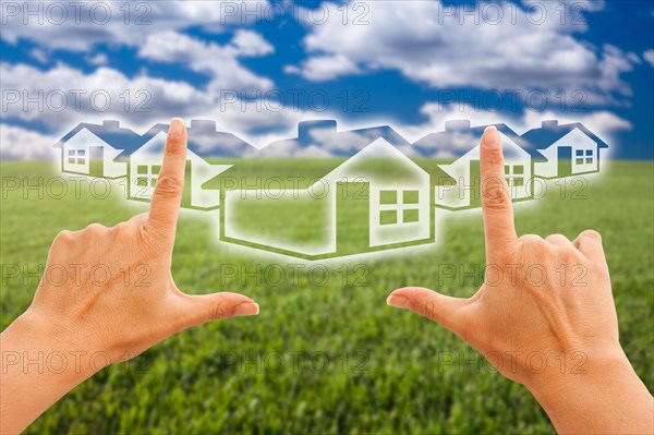 Female hands framing houses over grass field and sky
