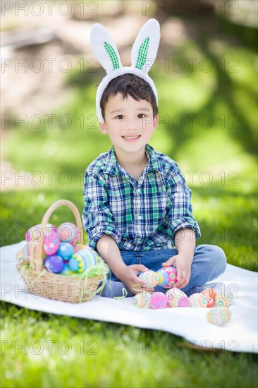 mixed-race chinese and caucasian baby boy outside wearing rabbit ears playing with easter eggs