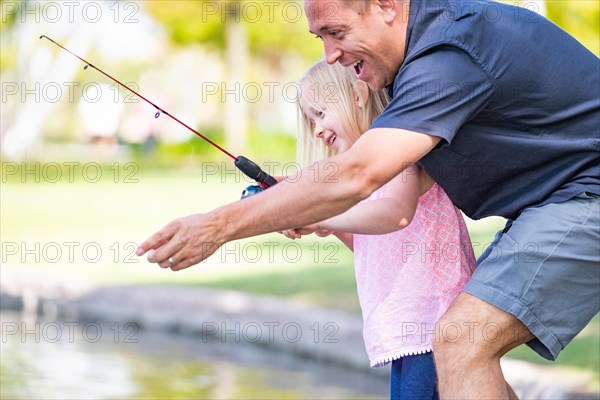 Young caucasian father and daughter having fun fishing at the lake