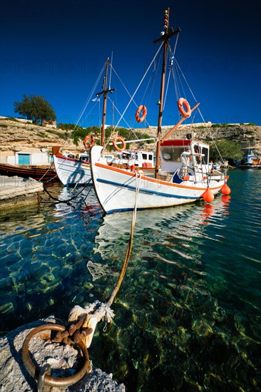 Fishing boats moored in crystal clear turquoise sea water in harbour in Greek fishing village of Mandrakia