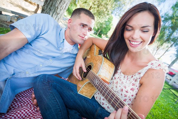 Young adult girl playing guitar with boyfriend in the park